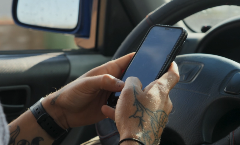 Male hands with tattoos texting while driving.
