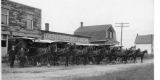 A row of eight horse-drawn carts line up in front of the bakery building.